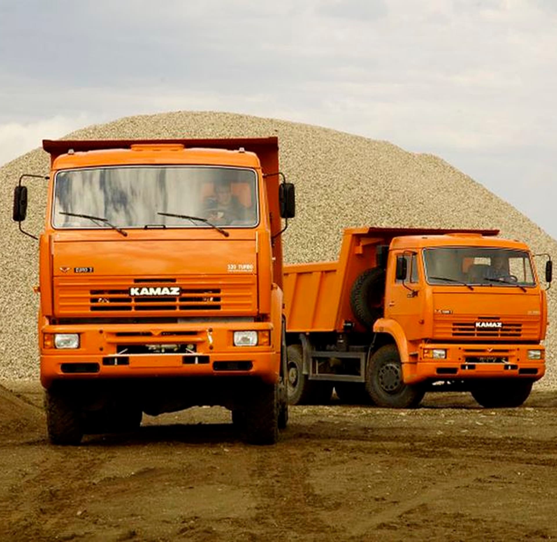 Orange dump trucks parked at a gravel yard